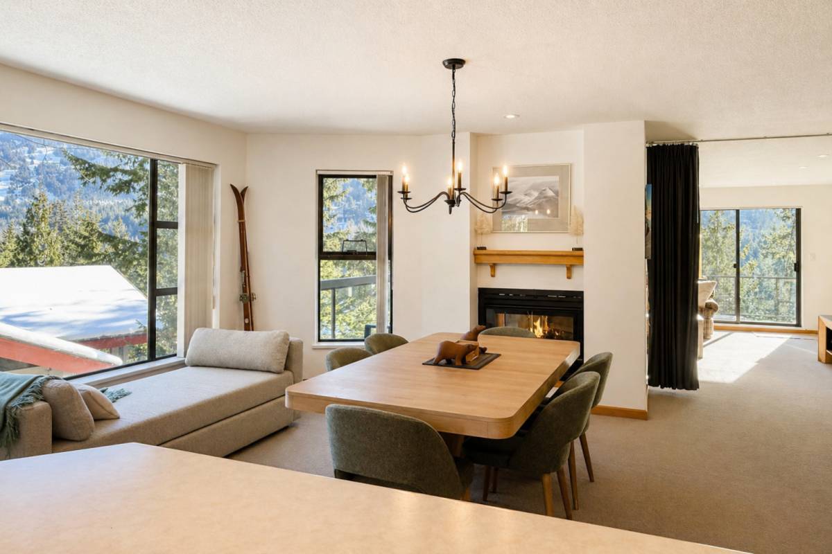 The dining and family room off the kitchen, with a large table, a double-sided gas fireplace, and a cushioned window seat under a wide window framing the mountains.