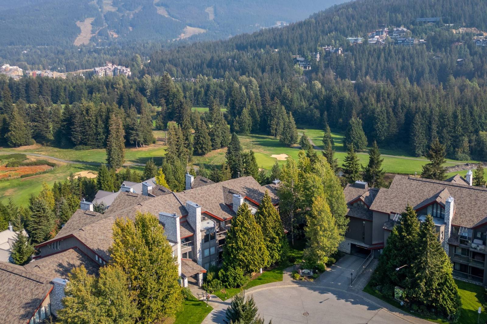 Aerial view of the Greyhawk building beside Whistler Golf Course, with the ski runs, gondola, and Whistler Village visible in the distance.