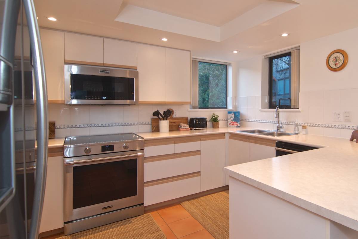 The kitchen with white cabinetry, a new stainless induction stove, an over-range microwave, and long stretches of counter and cupboard space.