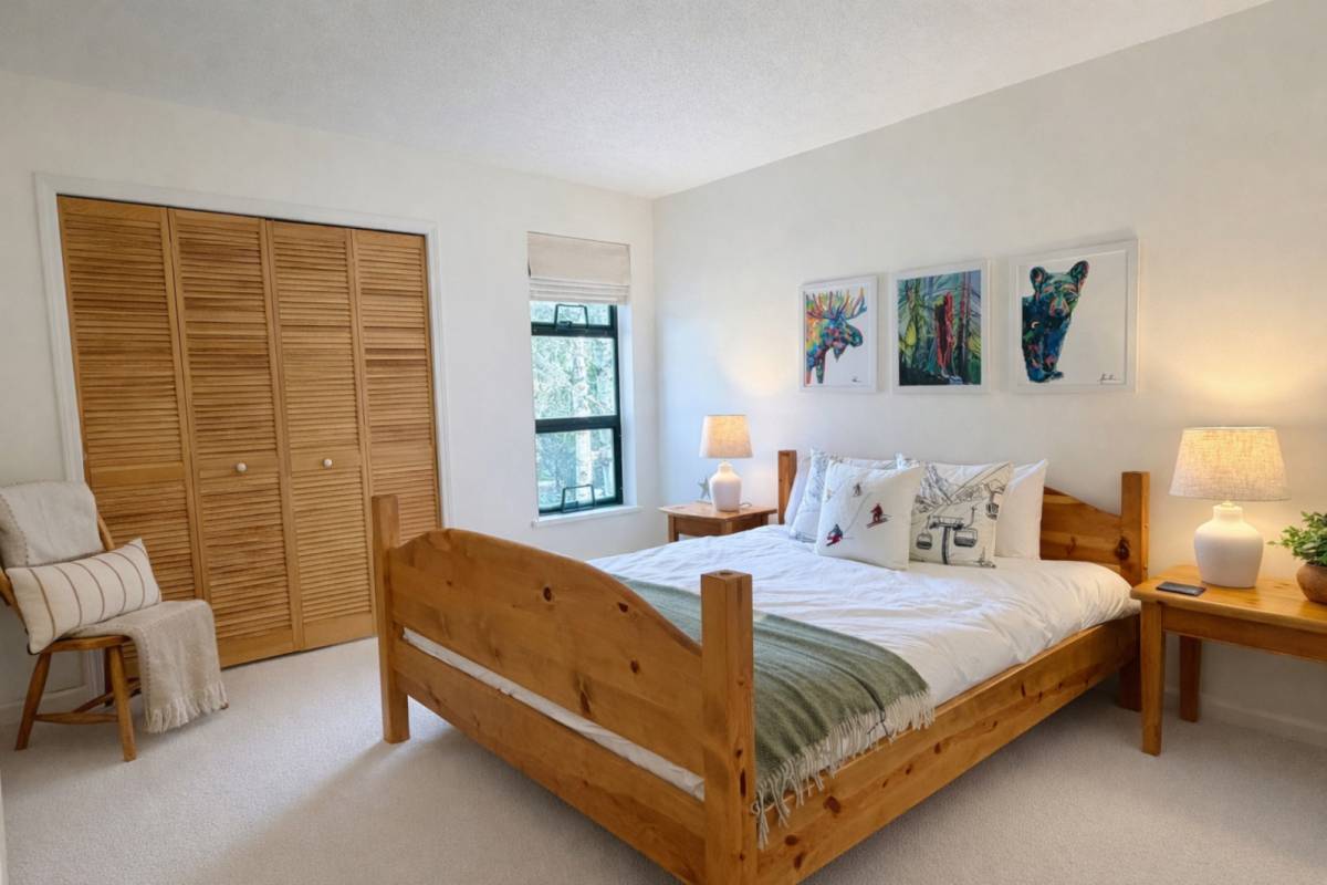 The second bedroom with a queen bed in a wood frame, a full louvered closet, and framed wildlife prints.